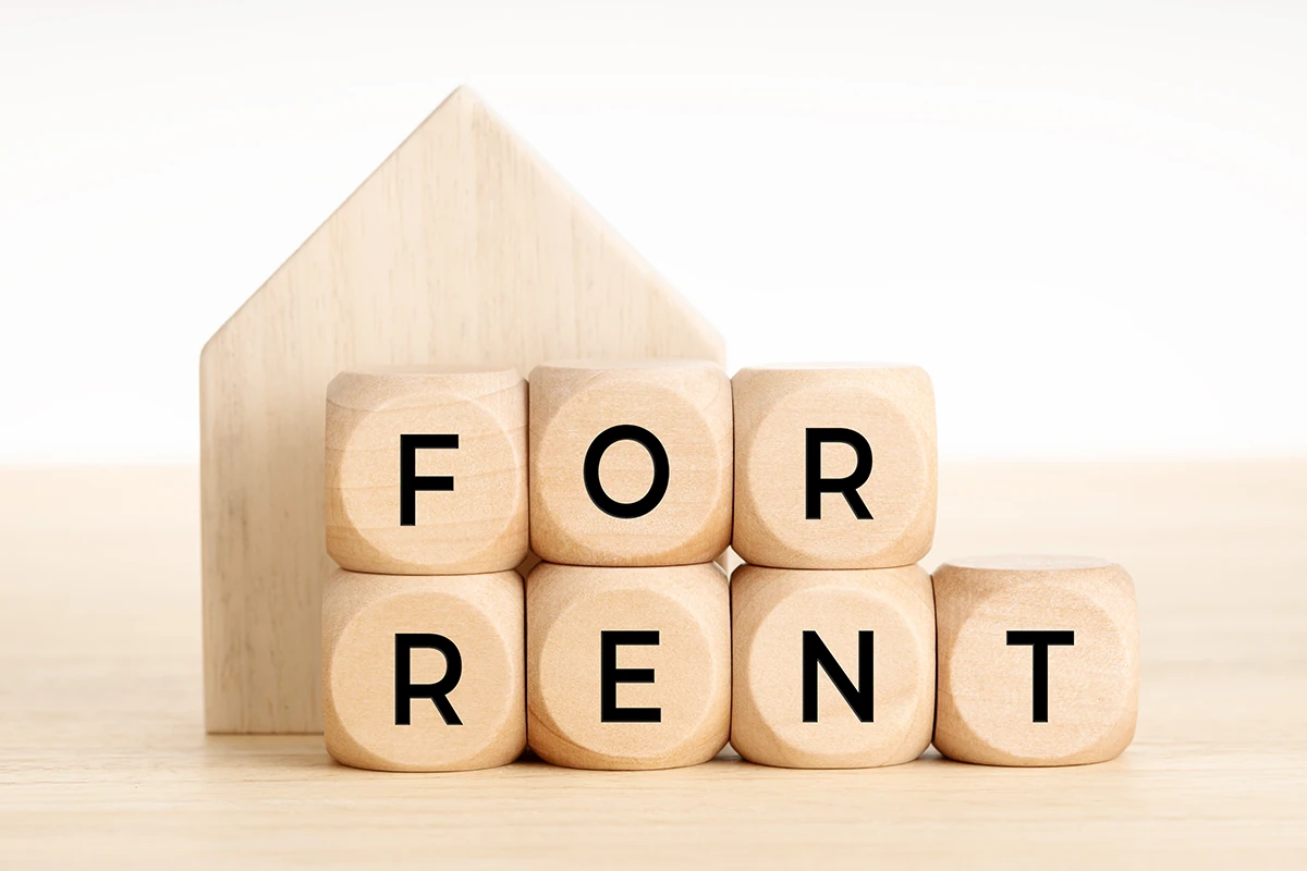 Wooden blocks spelling For Rent in front of a wooden house cutout